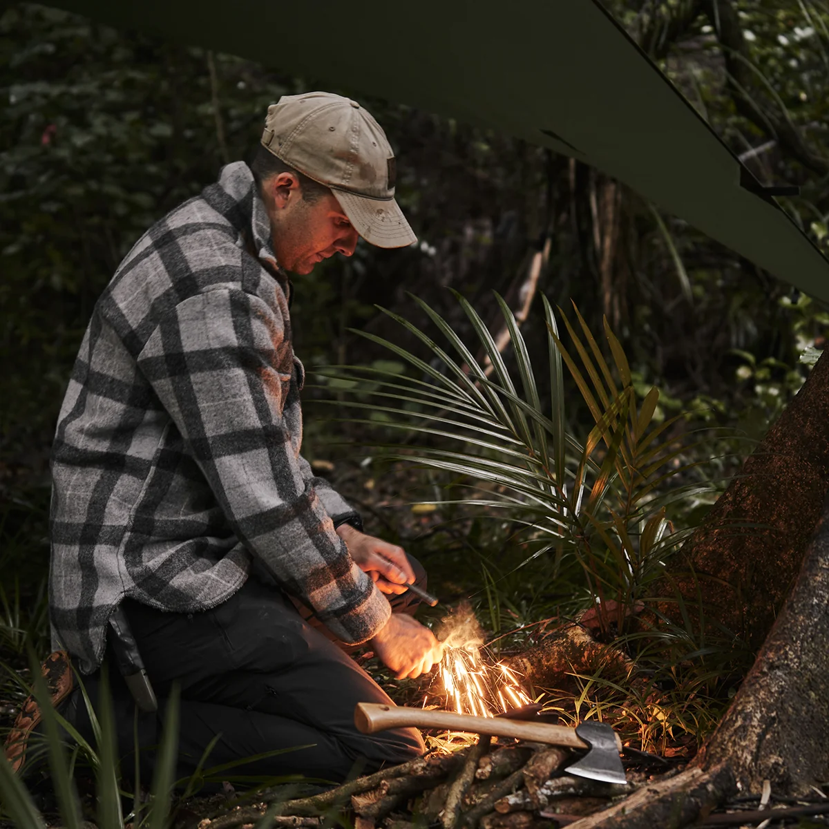 Outdoorsman striking ferro rod to start fire at campsite. A shower of sparks is shown falling into tinder material.