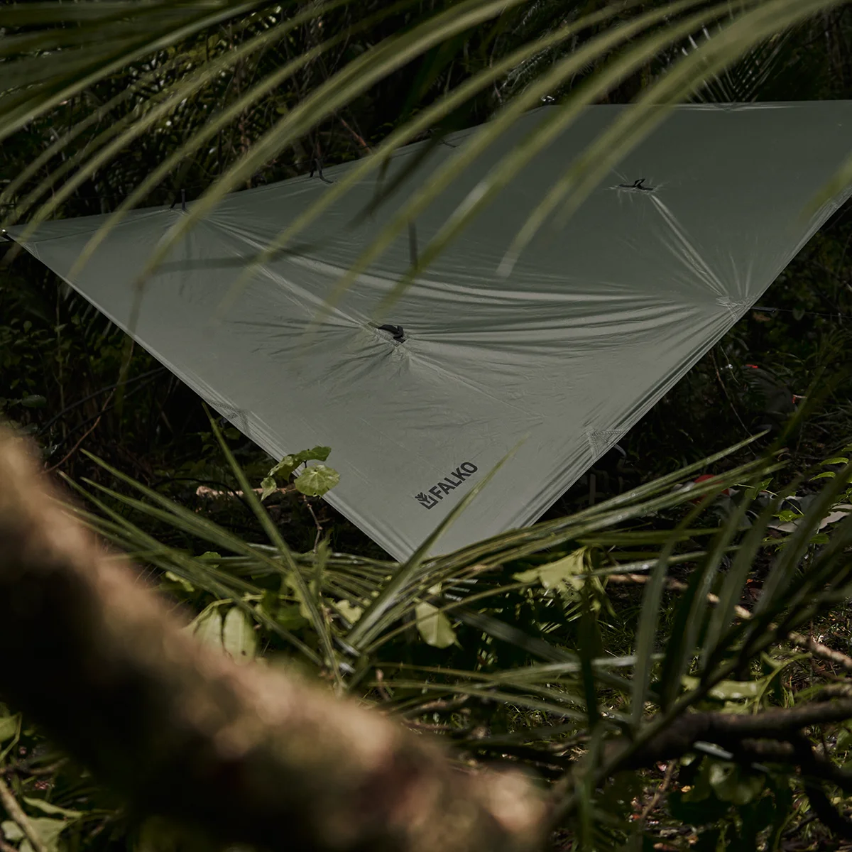 The Falko 'Vast' Silnylon camping tarp strung between trees in the forest.